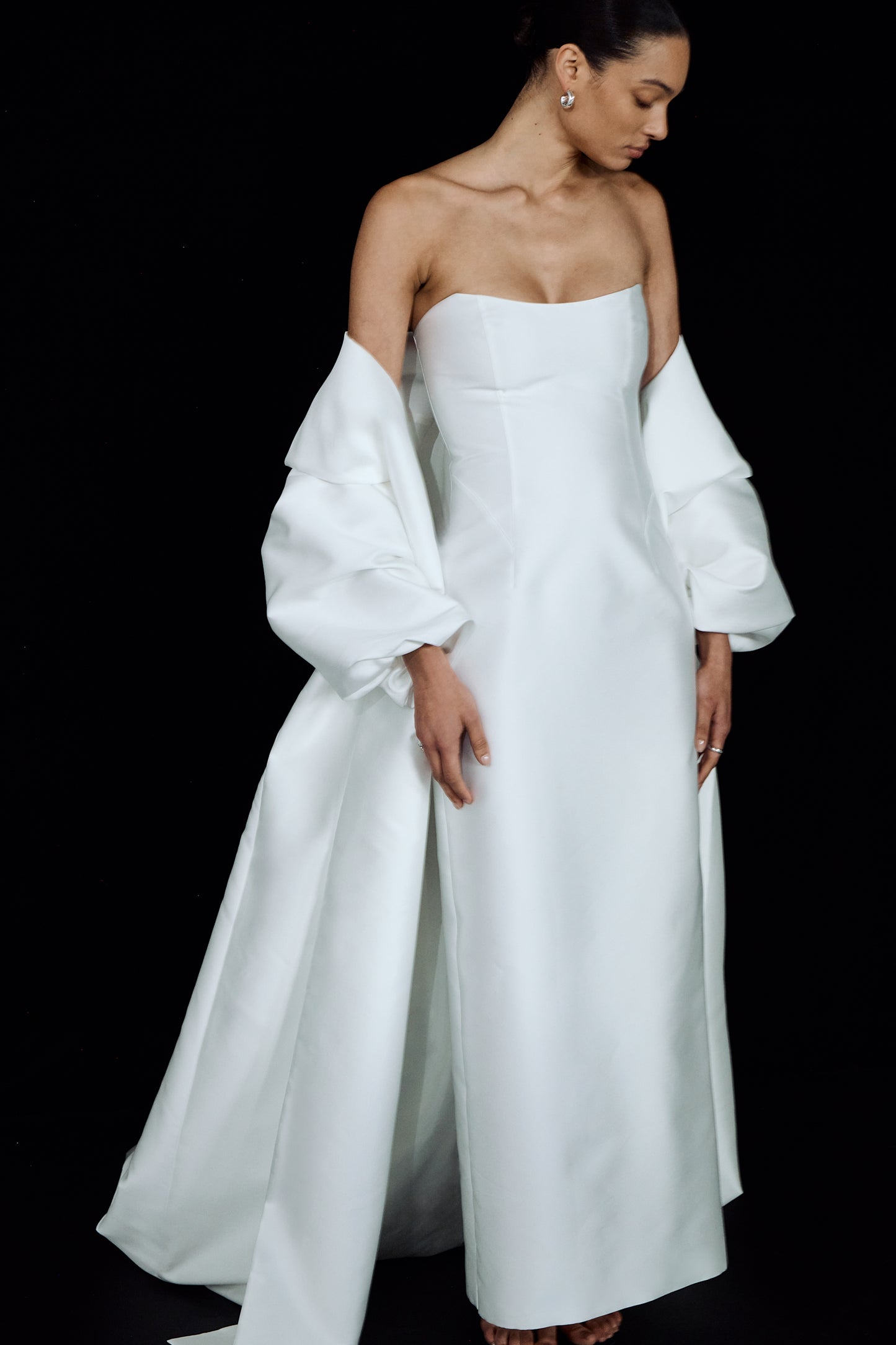 A minimalist, strapless wedding gown styled with a flowing white opera cloak that drapes over the arms.