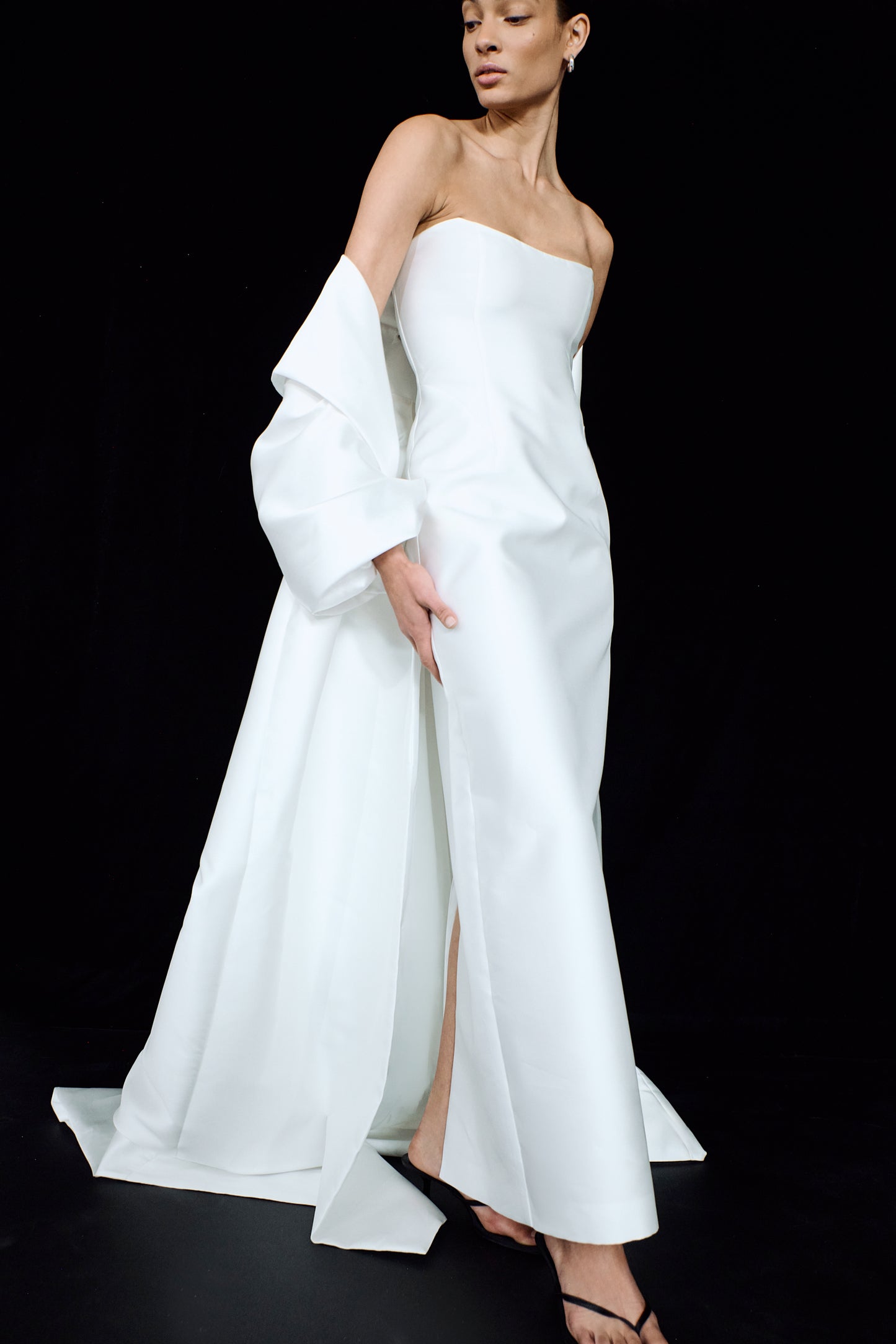 Side view showing a minimalist strapless bridal gown, worn with a flowing opera cloak.
