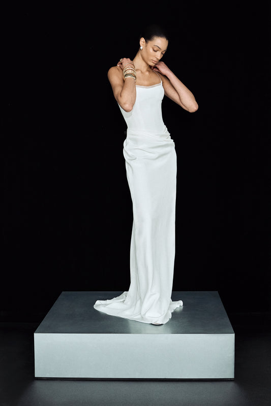 Full length image showing a minimalist white wedding dress, with draping at the hips and a flowing skirt
