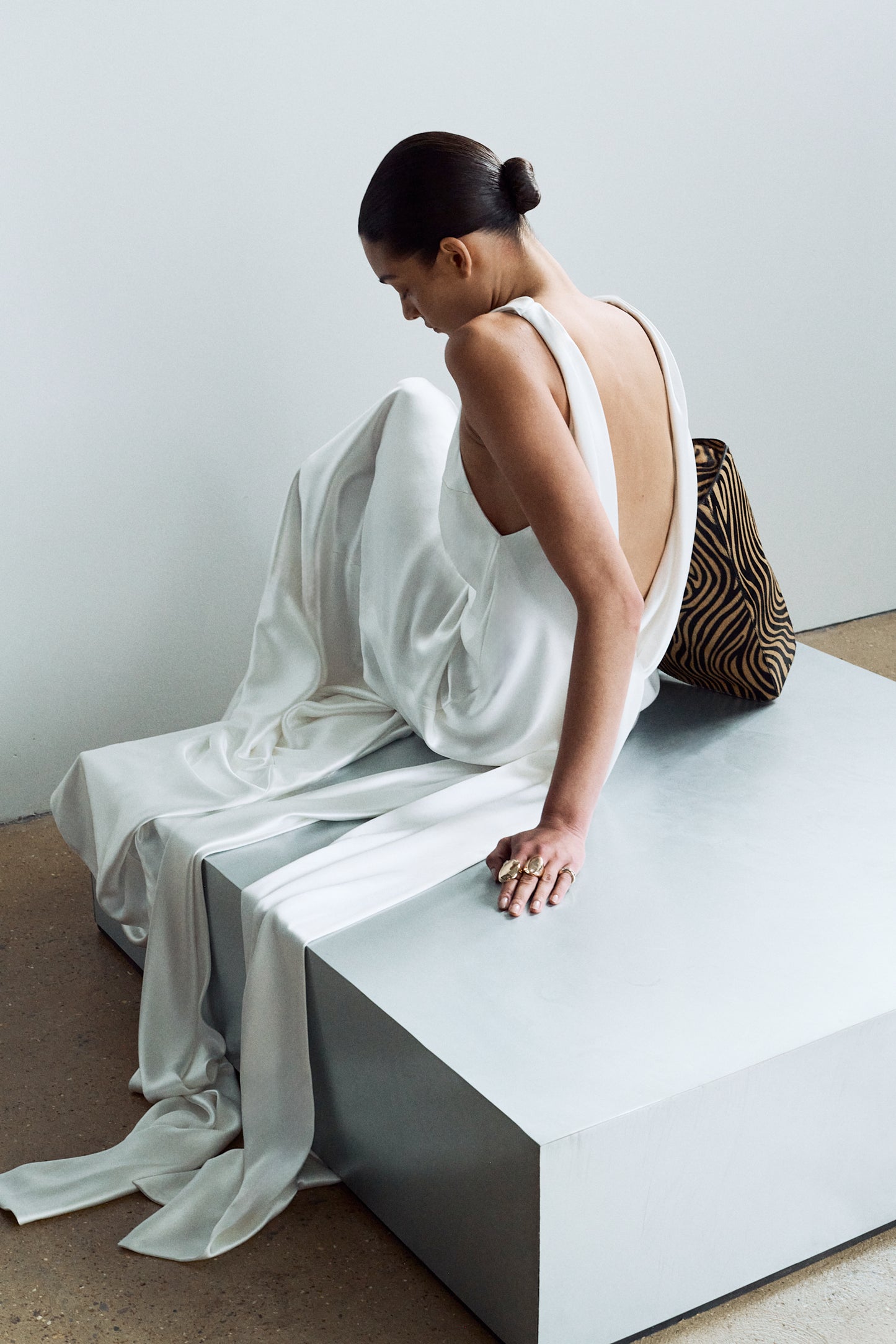 Model sitting, wearing an elegant white backless wedding dress with sash ties