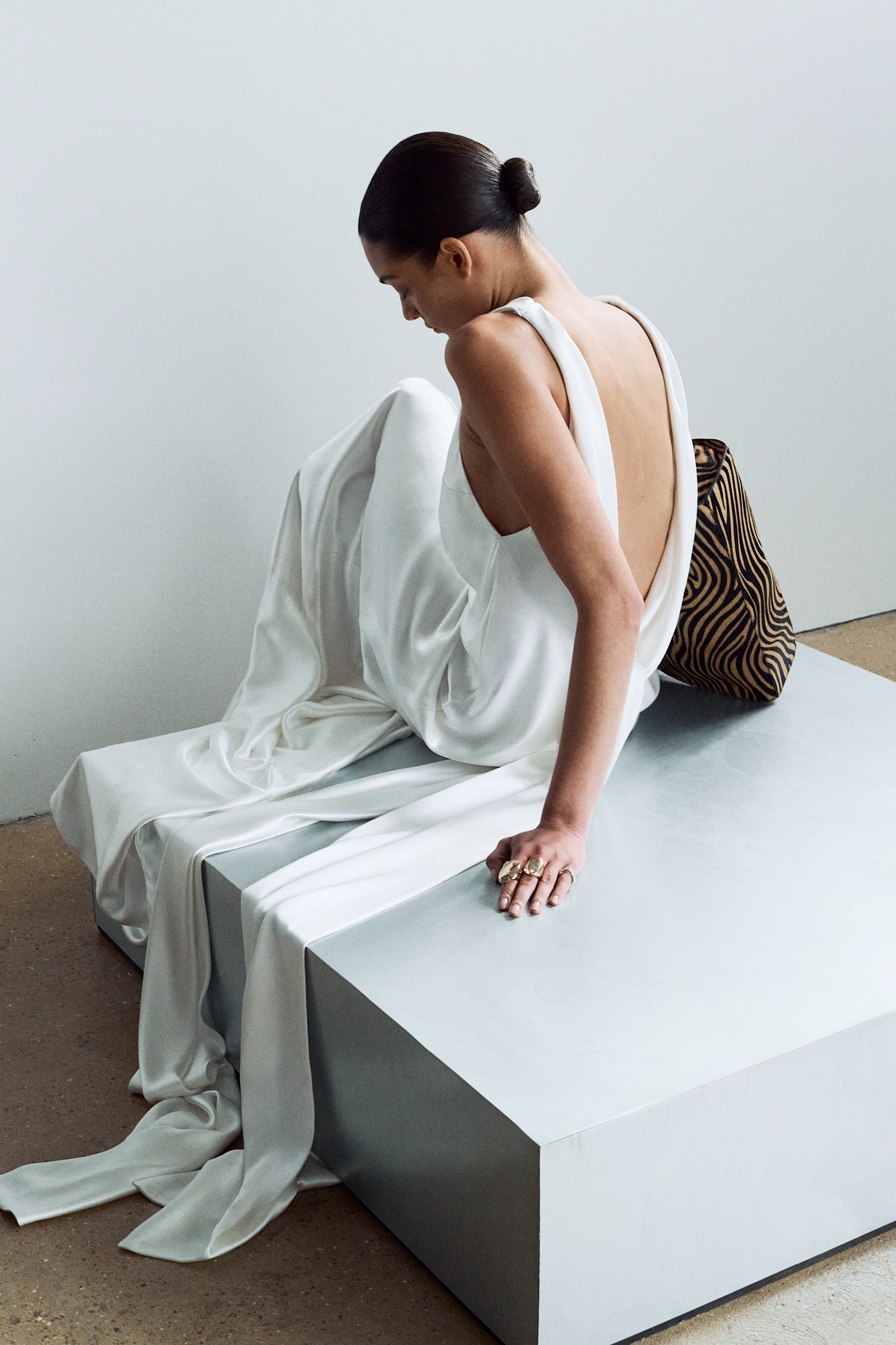Model sitting, wearing an elegant white backless wedding dress with sash ties