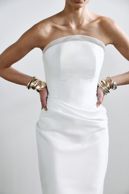 Sculpted crescent bridal gown with internal corset detailing and an elegant drape, styled with modern accessories