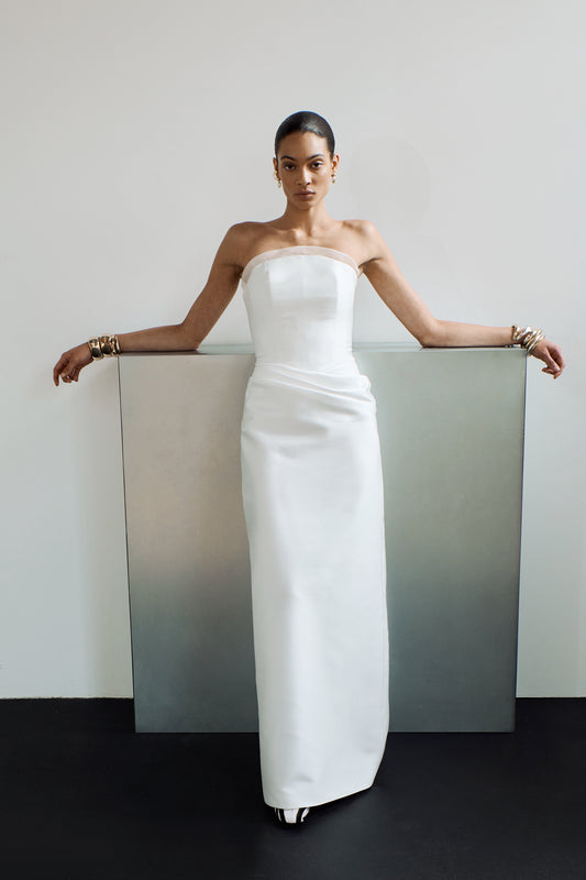 Front view showing a column wedding dress with a crescent neckline with organza detailing, and an elegant drape at the hip