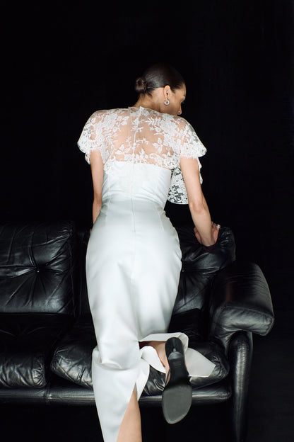 Back view showing a minimalist white gown, worn with a delicate lace mantle